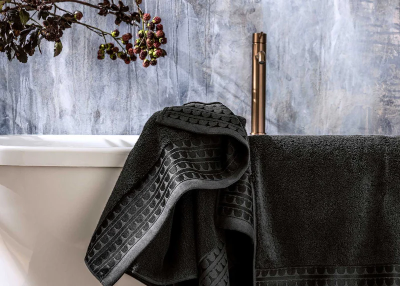 Une serviette de bain gris posée sur le rebord d'une baignoire blanche dans une salle de bain