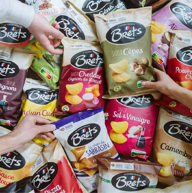 sachets de chips de la marque française Brets disposés côte à côte, avec des mains qui attrapent certains paquets